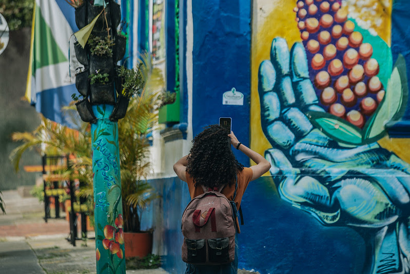 Fotografía de una mujer fotografiando un mural con su celular